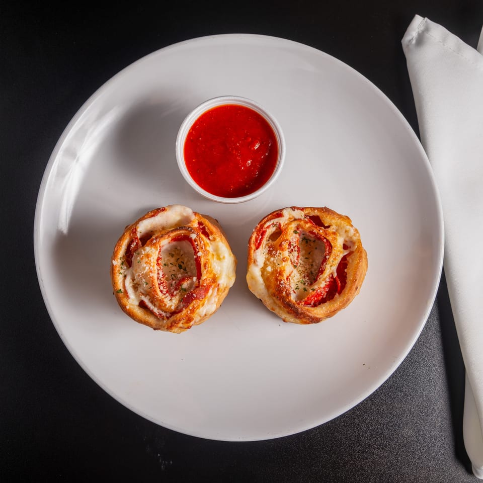 Two cheesy pepperoni pizza rolls served with marinara sauce on a white plate beside folded napkins.