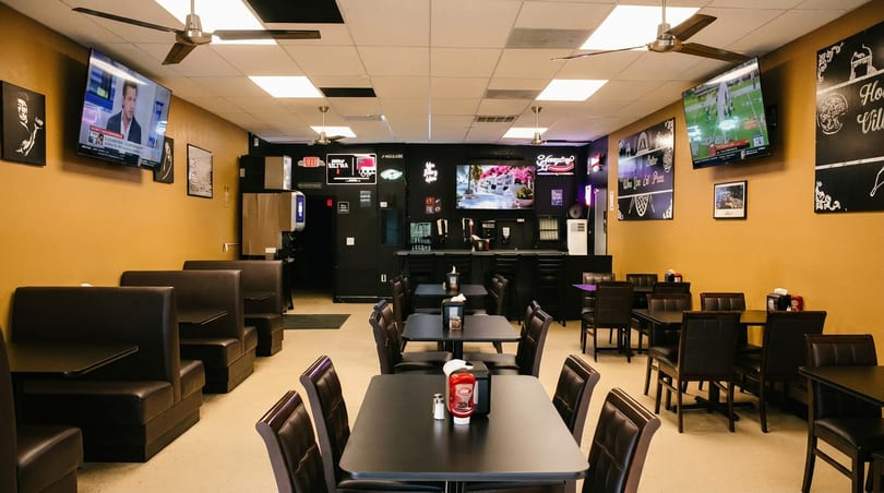 Casual restaurant interior with yellow walls, black booths, tables, and multiple TVs.