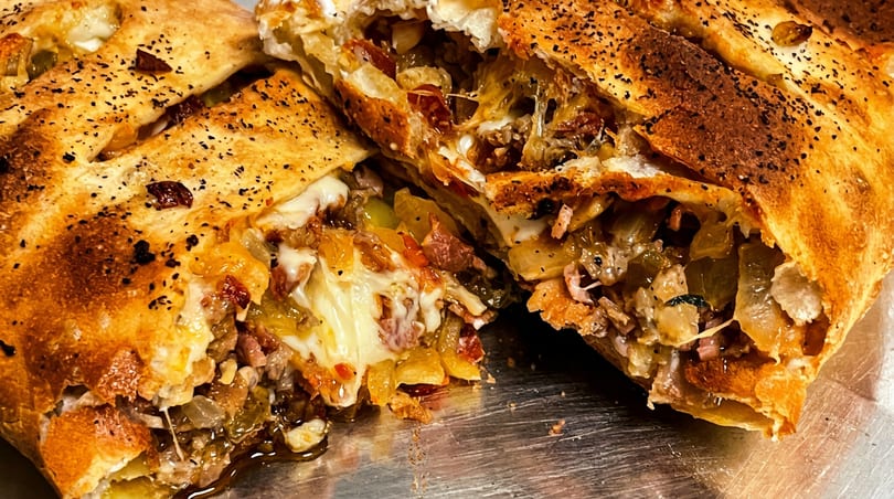 Golden-brown calzone sliced open, revealing gooey melted cheese, meat, and caramelized onions.
