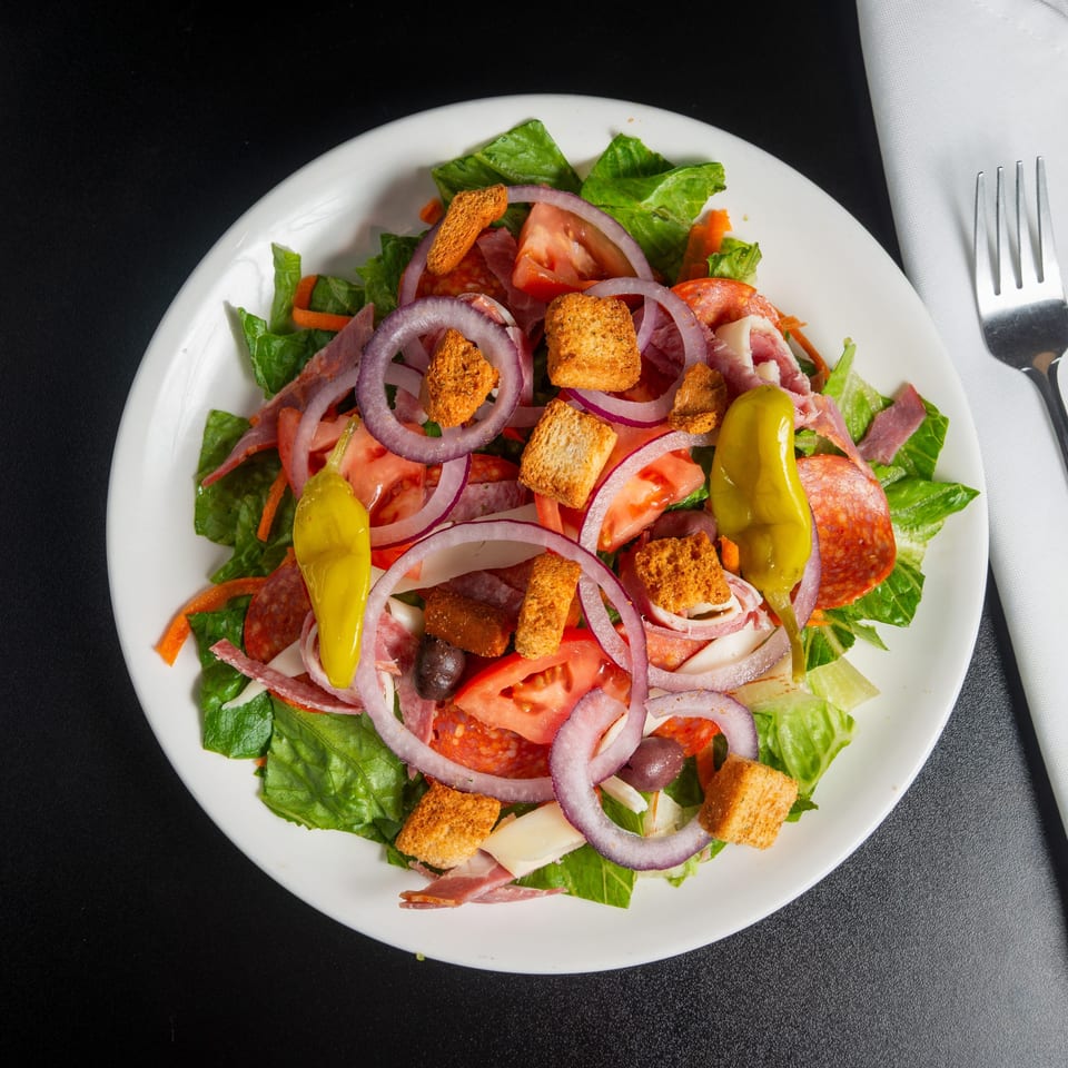 Overhead view of a loaded Italian salad with lettuce, tomatoes, onions, peppers, olives, cured meats, cheese, and croutons.