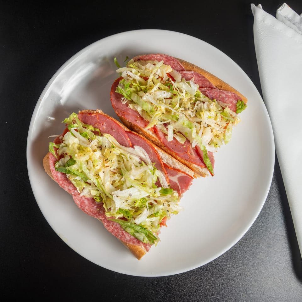 Two open-faced salami sandwiches topped with shredded lettuce on a white plate beside a folded napkin.