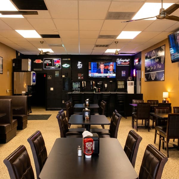 Spacious restaurant interior with dark booths, tables, and a bar, featuring yellow walls and multiple TVs.