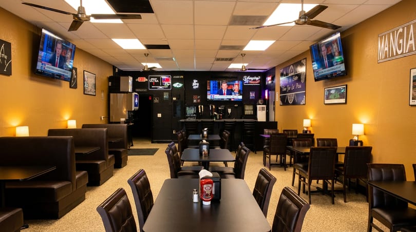 Cozy restaurant interior with brown booths, black tables, wall-mounted TVs, and a bar.