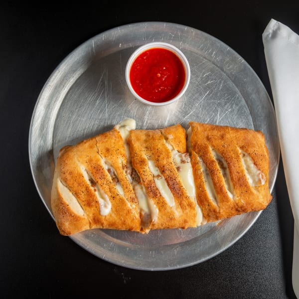 Sliced, golden-brown cheesy stuffed bread served on a metal platter with a cup of red dipping sauce.