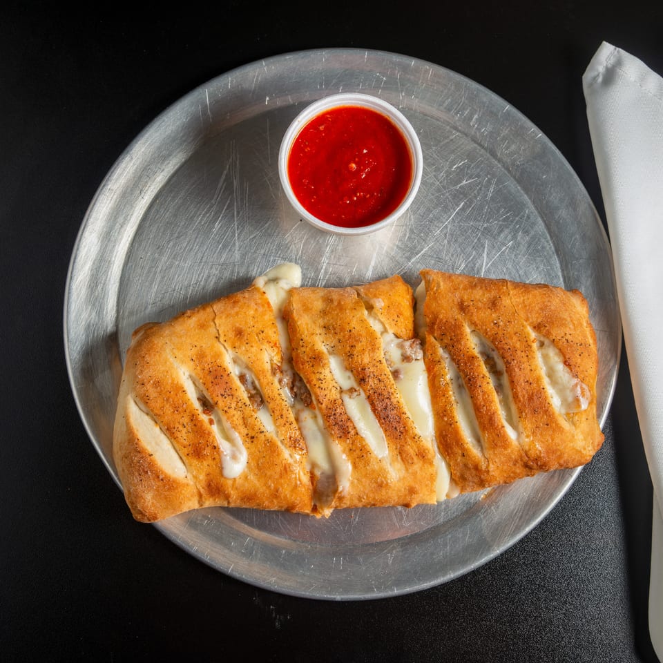 Sliced, golden-brown cheesy bread served on a metal platter with a cup of red dipping sauce and white napkin.