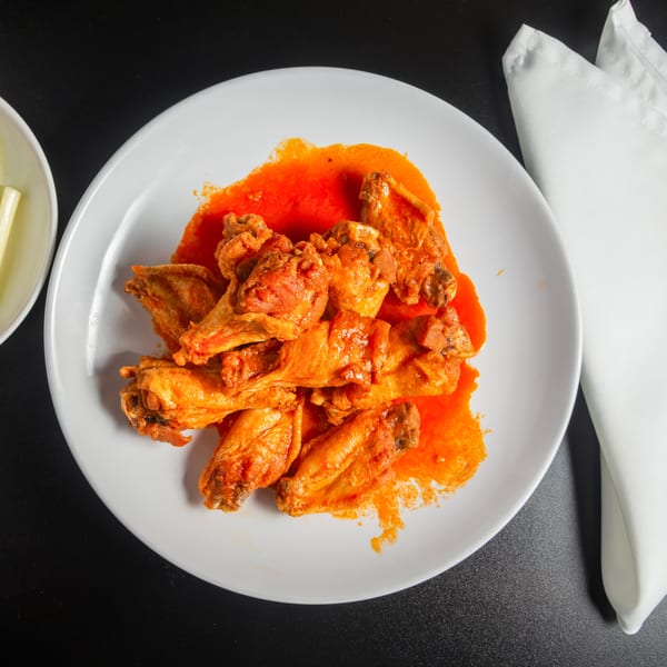 Crispy chicken wings coated in bright orange hot sauce, served with celery and carrot sticks on a white plate.